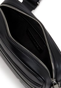 Black leather bag with silver zipper, featuring a smooth texture and compact rectangular shape. Interior is black fabric with a label visible.