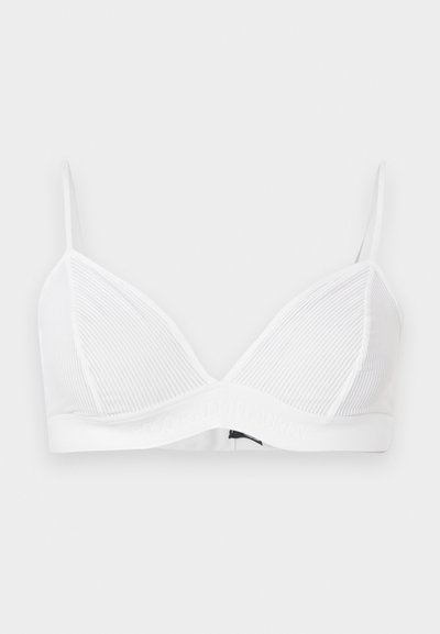 Λευκό ριμπ τριγωνικό σουτιέν με λεπτές ρυθμιζόμενες τιράντες και ελαστική ταινία κάτω, σε απλό ανοιχτό γκρι φόντο.