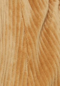 Tissu en velours côtelé de couleur beige clair avec une texture côtelée verticale et une couture visible traversant le matériau en diagonale.