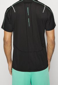 Černé sportovní tričko s krátkým rukávem, šedými akcenty na ramenou a texturovaným švem, který vede svisle po zádě.