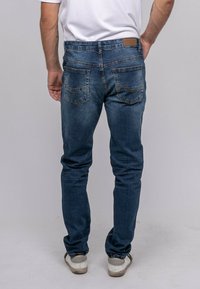 Jean en denim bleu avec une coupe slim, dotés de poches arrière avec des coutures décoratives et d'une patch en cuir avec logo sur la taille.