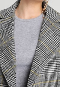 Grå rutig kavaj med hounds-tooth-mönster och gula accenter, parat med en grå crew neck t-shirt under.