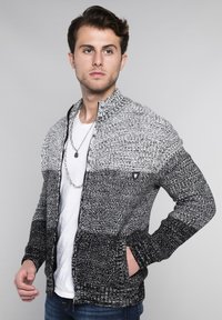 Strickjacke mit Reißverschluss in Schwarz- und Grauverlauf. Merkmale sind ein hoher Kragen, seitliche Taschen und ein Logo auf der linken Brustseite.
