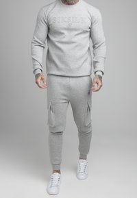 Sudadera gris con el logo "SIKSILK", combinada con pantalones cargo grises a juego que cuentan con bolsillos laterales. Zapatillas blancas completan el look.