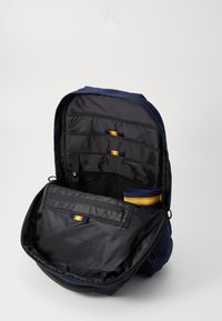 Zaino navy con interno nero, dotato di scomparti multipli, strisce orizzontali rosse e gialle e una tasca con zip.