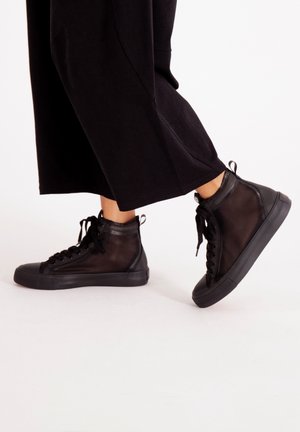 Zapatillas altas negras con parte superior de malla, puntera redonda y suelas de goma con detalles texturizados y cordones.