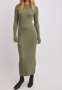Robe en maille côtelée vert olive avec manches longues et silhouette ajustée. Portée avec des bottines noires à bouts carrés.