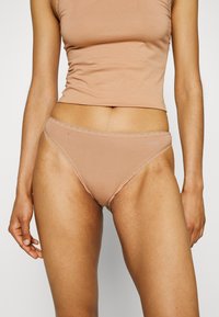 Tan bikini-briefs i mjukt, elastiskt tyg med spetsdetaljer. Har en klassisk skärning och subtil logotypdetalj på midjebandet.
