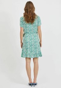 Grön blommig klänning med korta ärmar, rynkad midja och utsvängd kjol. Har ett mönster av små, färgglada blomblad och en slät textur.