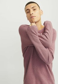 Lange mouwen, textuurtrui in licht mauve, met een relaxte pasvorm en oversized mouwen. Naaddetails voegen subtiele visuele interest toe.
