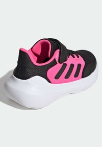 Black and pink athletic shoe with a mesh upper, padded collar, velcro strap, and a white cushioned sole; features three black stripes on the side.