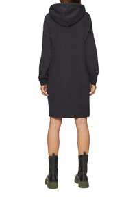 Schwarzes Kapuzensweatshirtkleid mit langen Ärmeln, einer lässigen Passform und einem leicht ausgefransten Saum, kombiniert mit schwarzen und grünen klobigen Stiefeln.