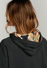 Czarna bluza z kapturem. Posiada podszewkę z kwiatowym wzorem wewnątrz kaptura. Miękka tekstura, luźny krój i rękawy raglanowe.