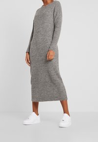 Grå stickad klänning med långa ärmar och rund halsringning, med rak passform och mjuk textur, tillsammans med vita sneakers.