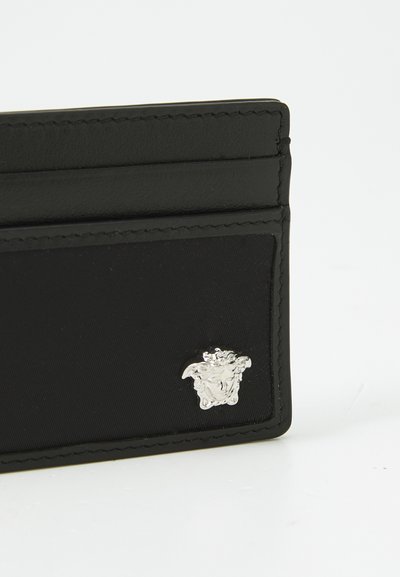 Black cardholder made of smooth leather with a silver Medusa emblem. Features slots for cards and a stitched border detail.