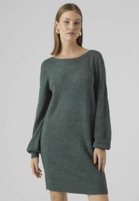 Abito grigio lavorato a maglia con scollatura ampia, maniche lunghe a sbuffo e vestibilità morbida. Tessuto morbido e lunghezza fino a metà coscia. Nessun motivo o accessorio visibile.