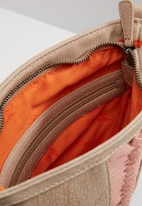 Interno di una borsa in pelle beige con rivestimento in tessuto arancione e tasca con zip, dotata di un esterno texturizzato e bordi lisci.