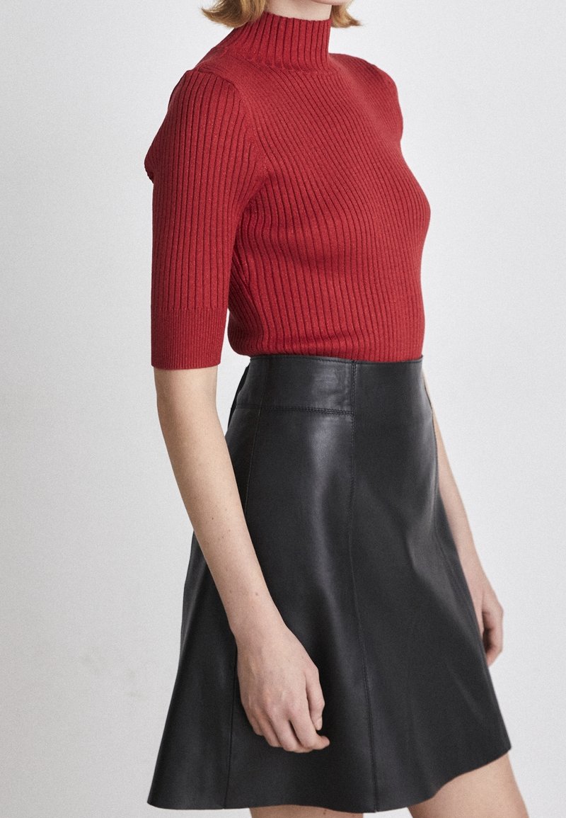Röd ribbad stickad kortärmad polotröja i kombination med en svart läderkjol med utsvängda delar. Fokusera på textur och kontrasterande material.
