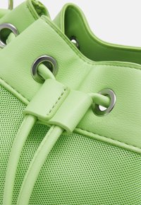 Borsa a sacco in rete verde chiaro e pelle con occhielli in metallo e fermo in pelle cucito per il cordoncino.