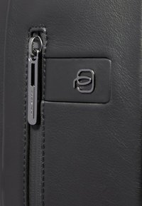 Zwarte leren portemonnee met een strak ontwerp, gladde textuur en een zilverkleurige ritssluiting. Opvallend merkdetail op het oppervlak.