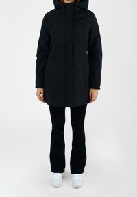 Černá zateplená parka s kapucí, s rovný střih, předním zipem a bočními kapsami. Nositelná přes černé kalhoty a bílé tenisky.