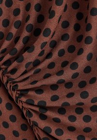 Brunt stof med et mønster af store sorte prikker og rynket tekstur. Blød og glat tekstur, der fremhæver stoffets fald.