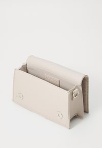 Sac en cuir beige pâle de forme rectangulaire, avec une fermeture à aimant et un seul compartiment intérieur. Présente un logo subtil à l'intérieur.