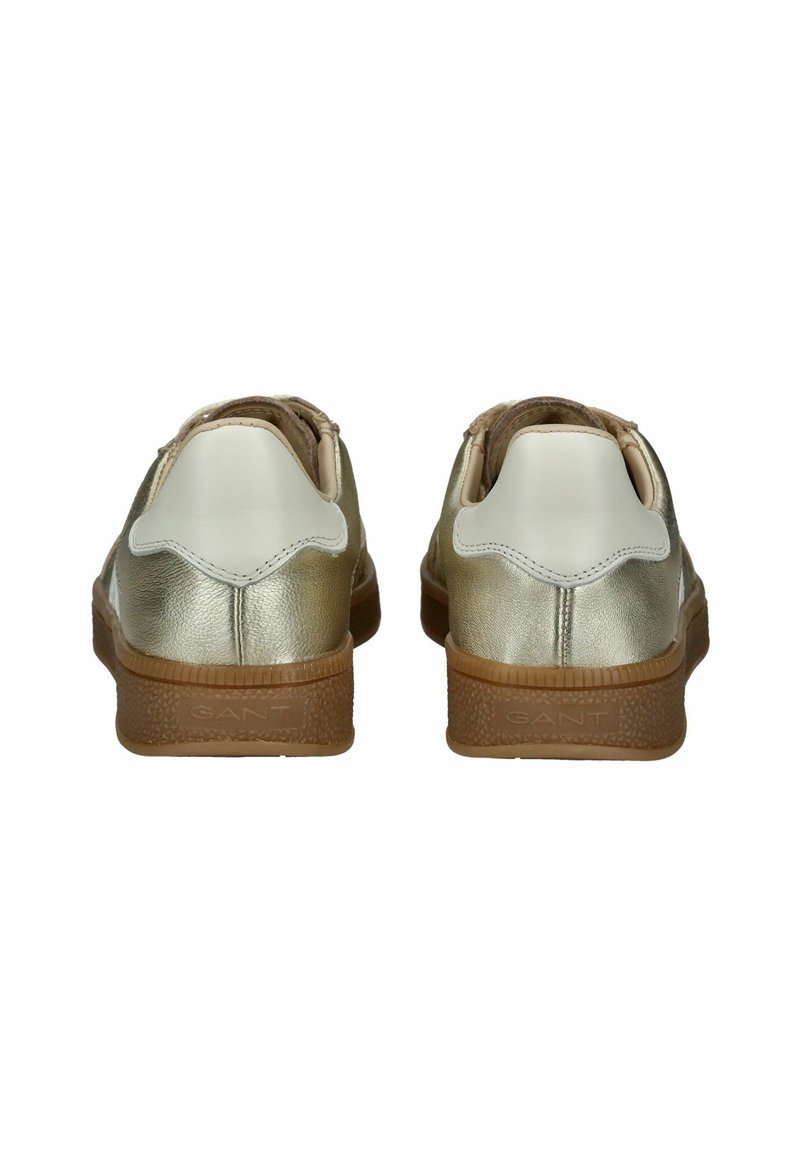 Chaussures en cuir métalliques dorées et blanches avec une semelle texturée marron, arborant un design festonné à l'arrière et une finition lisse sur le dessus.