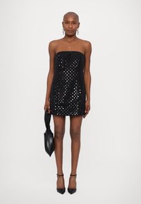 Rochie mini neagră, fără bretele, împodobită cu paiete strălucitoare, cu un design ajustat și o siluetă în formă de A. Modelul poartă o geantă neagră și tocuri.