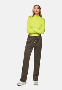 Long-sleeve, bright neon yellow top paired with brown, textured pants featuring a drawstring and neon side stripes. Gray athletic shoes.