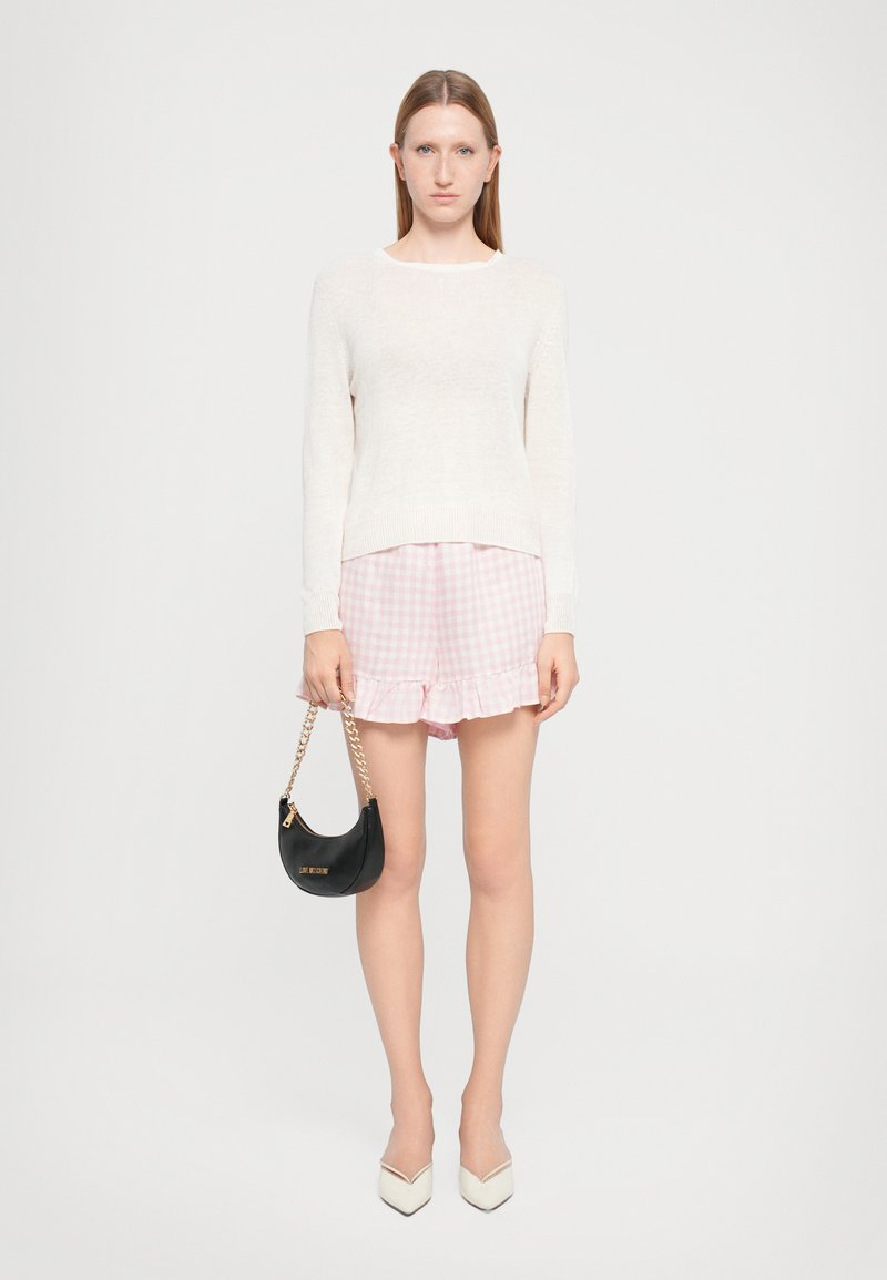 Ανοιχτό μπεζ πλεκτό πουλόβερ, ροζ καρό σορτσάκι με φρου-φρου, μαύρη τσάντα χειρός με αλυσίδα και λευκά παπούτσια στιλέτο.