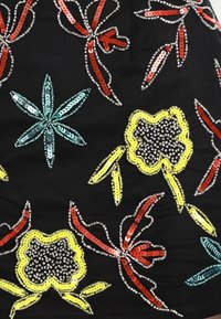 Svart tyg prytt med färgglada paljettblommönster i rött, gult, grönt och silver, med olika blomformer och texturer.