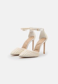 Scarpe bianche con tacchi alti e punta affusolata, caratterizzate da un design testurizzato simile a perle, cinturino alla caviglia regolabile e tacchi a spillo sottili.
