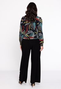 Pantalones de pierna ancha negros combinados con una blusa de estampado floral multicolor con mangas largas y puños elásticos.