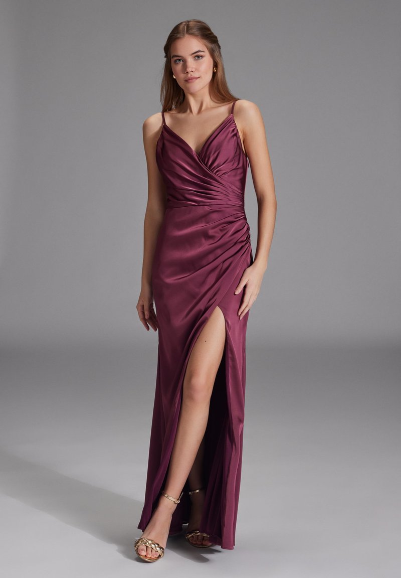Burgunderfarvet satin aftenkjole med tætsiddende bodice, draperede detaljer og en slids op til låret. Tynde spaghetti-stropper og glat tekstur.