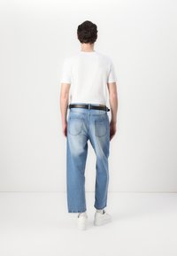 Jeans de mezclilla azul claro con un corte relajado, que presentan una cintura de altura media, bolsillos traseros y un cinturón negro, combinados con una camiseta blanca.