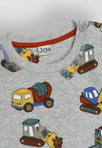 T-shirt in cotone grigio con motivi colorati di veicoli da costruzione, con scollo rosso e bottoni a pressione in plastica sulla spalla.