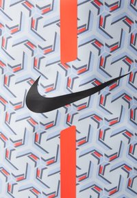 Producto de Nike que presenta una tela texturizada con un patrón geométrico combinando tonos de azul, rojo y negro, resaltado por un acento naranja y el logo.