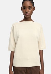 Jasnokremowy sweterek o luźnym kroju, szerokim dekolcie w łódkę i krótkich rękawach, z poziomym prążkowanym wzorem na całej powierzchni.