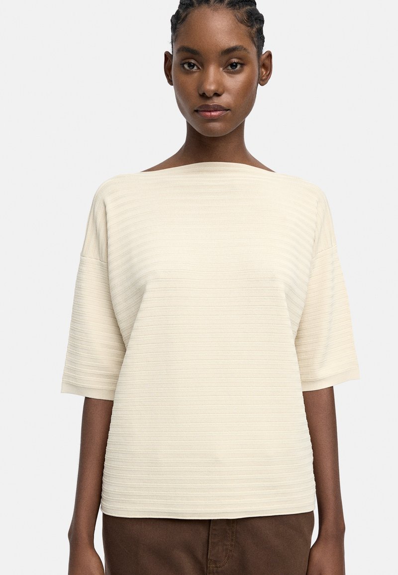 Jasnokremowy sweterek o luźnym kroju, szerokim dekolcie w łódkę i krótkich rękawach, z poziomym prążkowanym wzorem na całej powierzchni.