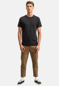 Zwarte katoenen t-shirt met een ronde halslijn, gecombineerd met tan chino's. Het model draagt zwarte sneakers met witte accenten en gestreepte sokken.