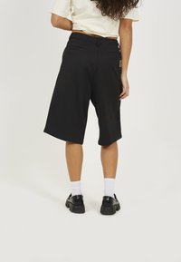 Black knee-length shorts with a smooth texture, featuring front and back pockets, and a fitted waistband, paired with chunky black shoes.