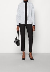 Camicia button-up a fiori blu chiaro, dolcevita nero, pantaloni neri, décolleté nere a punta e una piccola borsa a mano nera.