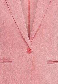 Blazer rouge présentant un tissu texturé, des revers à encoche, une fermeture à un bouton et deux poches avant avec des détails de couture subtils.