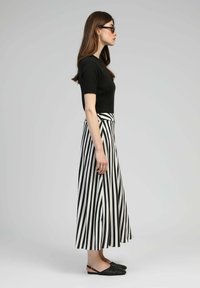 Haut noir à manches courtes côtelé, associé à une longue jupe rayée en noir et blanc. Les accessoires comprennent des chaussures noires à enfiler et une bague.