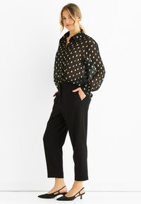 Sheer black blouse with gold leaf pattern, paired with tailored black trousers and pointed black slingback heels.