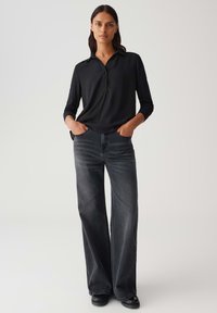 Polo shirt nero a maniche lunghe con colletto, abbinato a jeans in denim grigio a gamba larga. Entrambi i capi presentano una texture liscia e un fit casual.