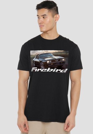 Junger Mann in schwarzem T-Shirt mit einem schwarzen klassischen Pontiac Firebird und dem Wort "Firebird" in weißer Schrift darunter.