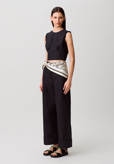 Top corto in cotone nero con maniche arricciate, abbinato a pantaloni larghi neri. Completano il look una sciarpa fantasia annodata in vita e sandali neri.