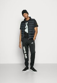Sort polstret vest over en grafisk sort t-shirt, parret med sorte sweatpants med "NIKE AIR" i hvid og sorte sneakers.